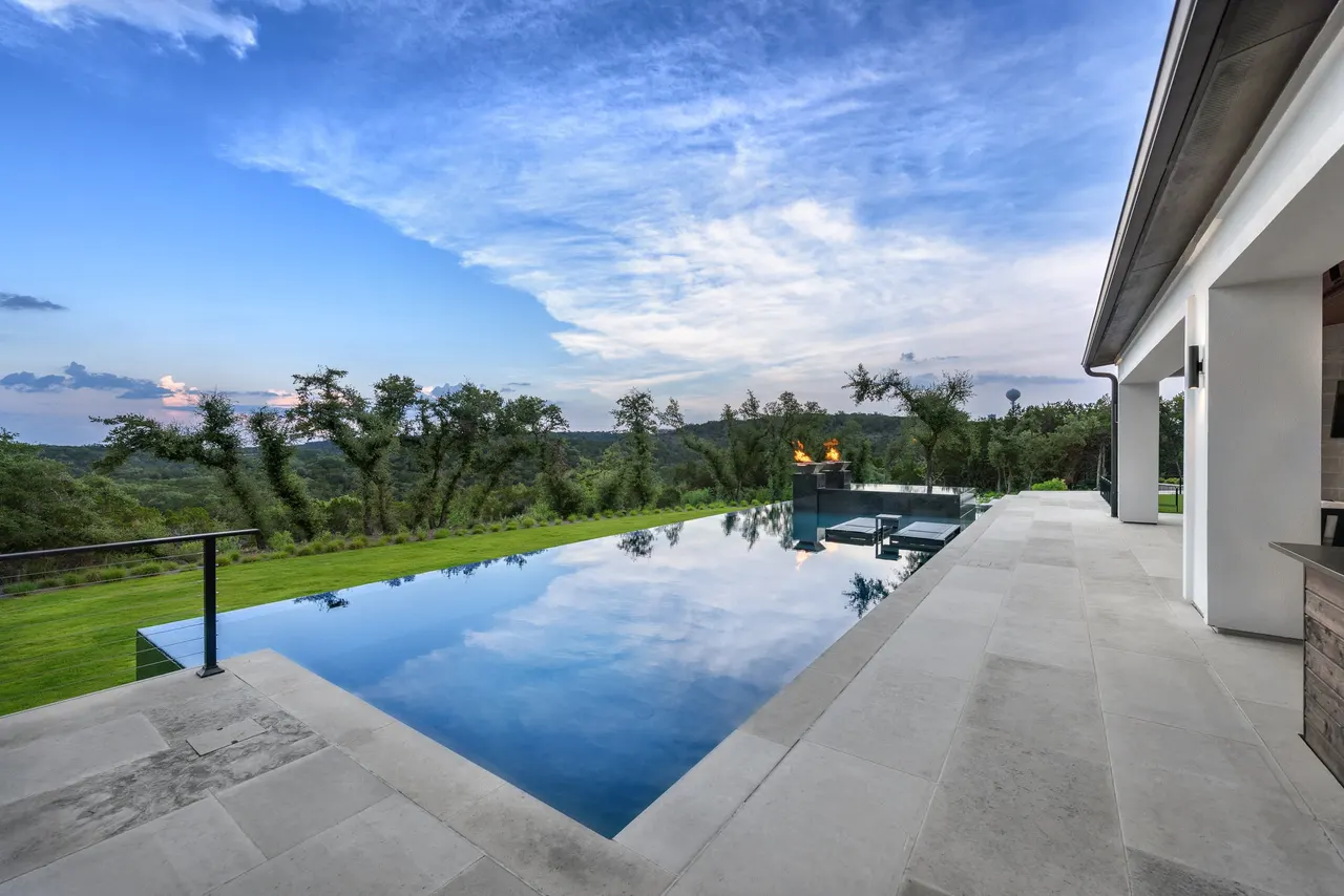 Estate infinity-edge pool with fire bowls and in-water lounge at dusk, Austin